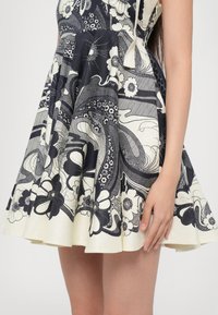 A-lijn jurk van gemusterde stof in navy en crème met bloemmotieven. De rok heeft een gladde textuur met subtiele plooien.