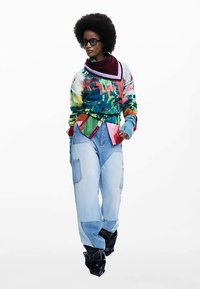 Farverig, mønstret trøje med høj hals, parret med lyseblå, oversize cargobukser og sorte, flæseankelstøvler.