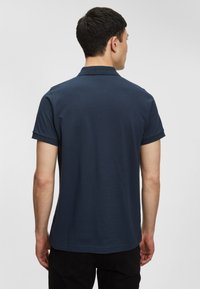 Námořnická modrá polo košile, krátké rukávy, klasický límec, žebrované manžety, měkká bavlněná tkanina, hladká textura, jednoduchý design.
