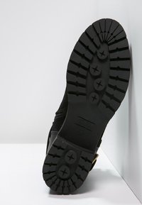 Black boot with a textured rubber sole, featuring a patterned tread, rounded toe, and a side zipper for closure.