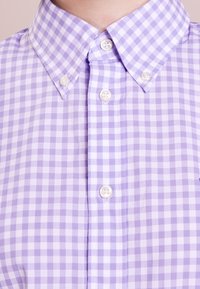 Nära bild av en lila och vit rutig skjortkrage med fyra synliga vita knappar.