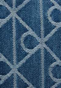 Ύφασμα από τζιν με γεωμετρικό μοτίβο σε λευκό χρώμα, με διασταυρούμενες γραμμές και κύκλους σε μπλε φόντο, που παρουσιάζει υφή επιφάνειας.