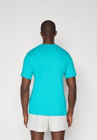 Turkusowa koszulka z krótkim rękawem, wykonana z bawełny, z okrągłym dekoltem, gładkim tyłem, zestawiona z jasnymi szortami.