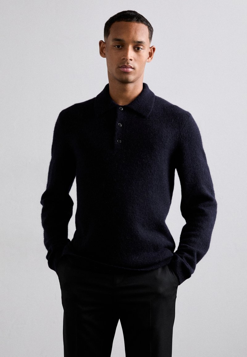 Dunkelblauer Strickpullover mit Kragen, ausgestattet mit einer Drei-Knopf-Verschluss, langen Ärmeln und einer weichen Textur, kombiniert mit schwarzen Hosen.