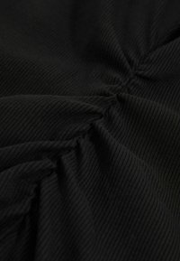 Material negru cu o textură nervată, având detalii plisate care creează pliuri și contururi moi. Materialul pare ușor și neted.