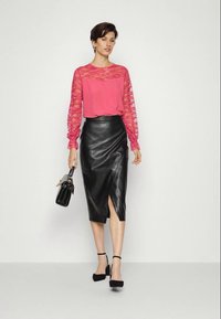 Blusa de renda rosa de manga longa com corpete sólido, combinada com uma saia justa de couro preta com uma fenda lateral. Acessorizada com uma pequena mala.