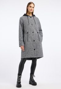 Grijze wollen blend jas met een zwarte capuchon, knoopsluiting, twee voorzakken en een middenlange snit, gecombineerd met zwarte nepleer leggings en laarzen.