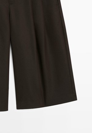 Mørkebrune vidde bukser med subtile lodrette nålestriber, synlig frontsyning og kantdetaljer på hvid baggrund.