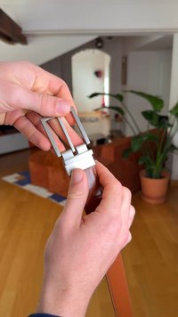 Ruskea nahkavyö hopeanvärisellä metallisoljella. Soljessa on kaksipiikkinen muotoilu, ja sitä pidetään kädessä.