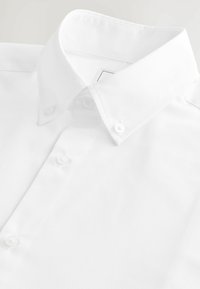 Chemise blanche à boutons avec un col écarté et quatre boutons sur la patte de boutonnage. Le tissu semble lisse et bien repassé.