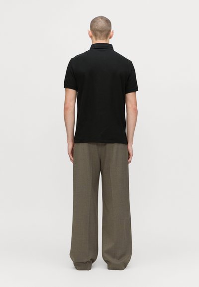 Black polo shirt with short sleeves, paired with loose khaki trousers. Smooth fabric, standard collar, minimalistic design.