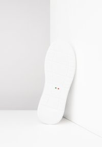Suola di sneakers bianche con modelli di grip testurizzati. Presenta una piccola bandiera italiana e un logo. Posizionata su uno sfondo chiaro.