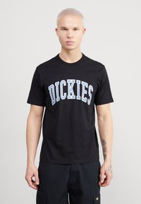 Černé bavlněné tričko s modro-bílým prohnutým logem "DICKIES" na hrudi. Krátké rukávy a klasický kulatý výstřih.