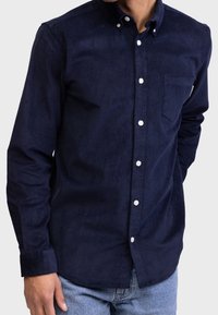 Navyblauwe corduroy shirt met een button-down kraag, witte knopen, een enkele borstzak en lange mouwen. Getextureerde stof met subtiele ribbel.
