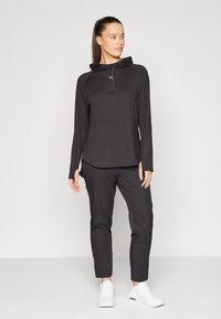 Black long-sleeve hooded top with a kangaroo pocket and drawstring, paired with tailored black pants and white athletic shoes.