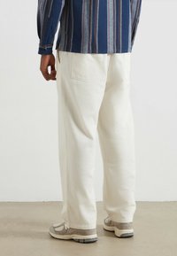 Białe spodnie o szerokich nogawkach wykonane z teksturowanej tkaniny, z tylnymi kieszeniami. W połączeniu z beżowymi sneakerami, prezentującymi swobodny, codzienny styl.