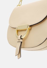 Beżowa skórzana torebka na ramię z złotym zapięciem i pasującym skórzanym frędzlem, z delikatnym przeszyciem wzdłuż brzegów.