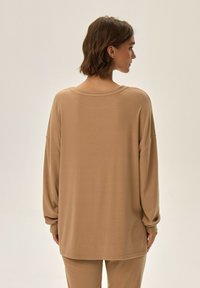 Luźna bluzka z długim rękawem w beżowym kolorze, z okrągłym dekoltem, opuszczonymi ramionami oraz gładką, lekką fakturą.