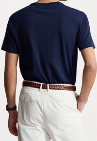 Navy blue short-sleeve t-shirt, cotton fabric, paired with white, tailored pants and a brown braided leather belt.