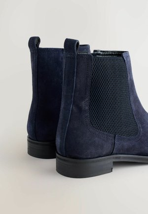 Donkerblauwe suède enkellaarsjes met textuurmesh zijpanelen, trekbands en een lage zwarte rubberen hak. Gladde afwerking met gestikte accenten.