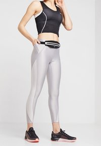 Crop top de sport noir avec des accents blancs, leggings gris clair avec des panneaux gris foncé, et baskets noires avec des semelles rouges. Banane à la taille.