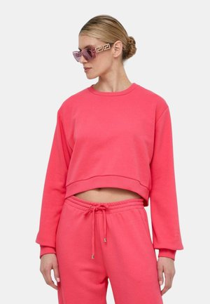 Felpa cropped rosa con maniche lunghe, abbinata a pantaloni jogger coordinati. Materiale in cotone morbido con vestibilità rilassata e vita elasticizzata.