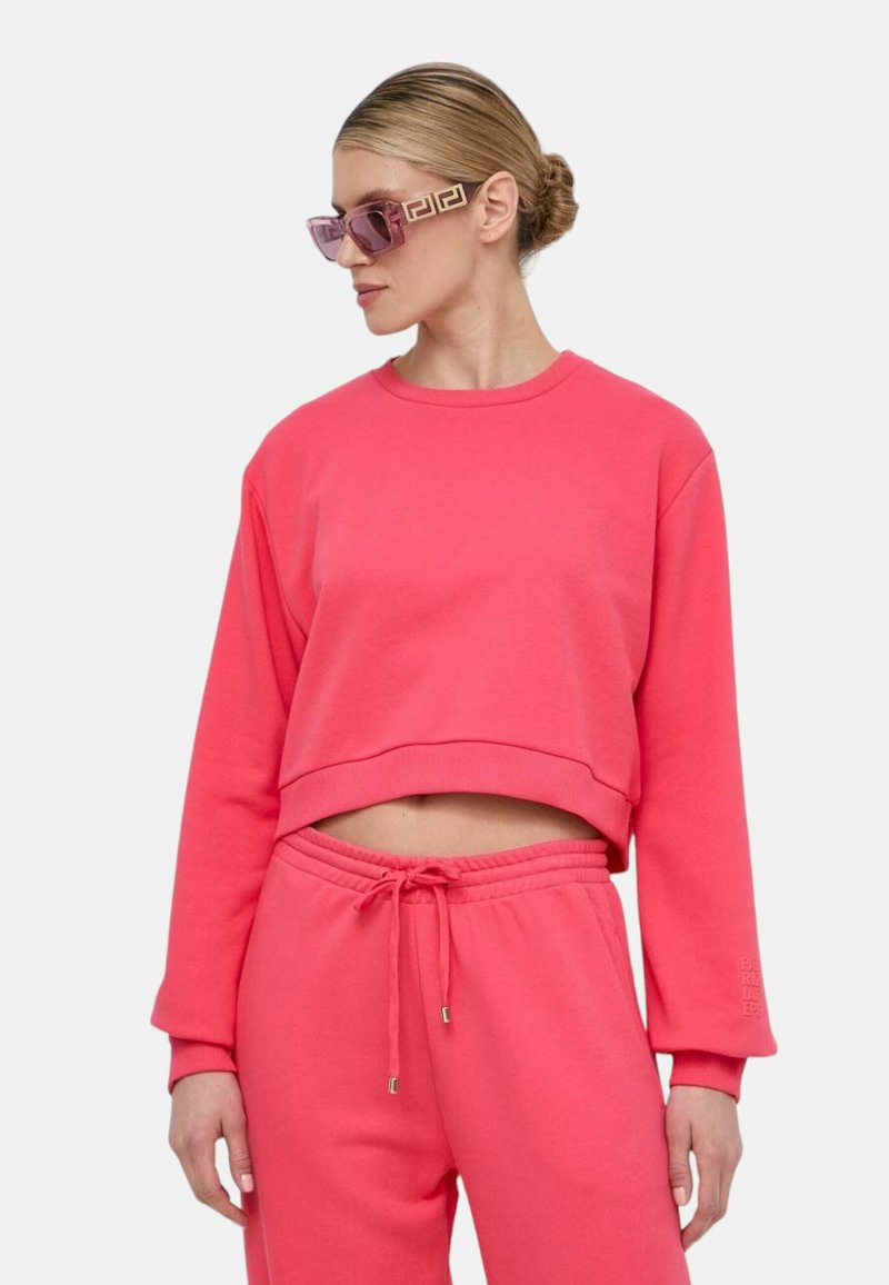 Felpa cropped rosa con maniche lunghe, abbinata a pantaloni jogger coordinati. Materiale in cotone morbido con vestibilità rilassata e vita elasticizzata.