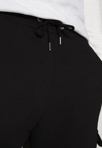 Zwarte joggingbroek met een trekkoord in de tailleband en metalen accenten. Gemaakt van zacht, textuurachtig materiaal en heeft een aansluitende pasvorm.