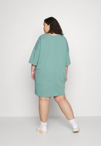 Vestido camisola verde oversized com decote redondo e mangas curtas. Tecido suave e corte reto, atingindo a metade da coxa, sem padrões.
