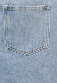 Ljusblå denimtyg med en sydd bakficka som har dubbel gulbrun tråd och förstärkta hörn.