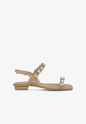 Beige platte sandaal met een lage hak, kruisbanden en decoratieve metalen studs. Heeft een verstelbare enkelband en een gladde textuur.