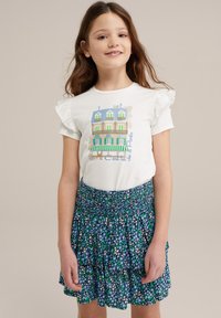 Balta t-krekla ar frill piedurkēm, uz kura ir krāsains ēku grafiks, apvienots ar zilu svārku ar ziedu rakstu un līmeņiem.
