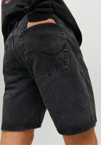 Mustat farkkushortsit, joissa on rento istuvuus, näkyvät saumat ja takataskut. Kangas on sileä ja siinä on hieman haalistunut pinta.