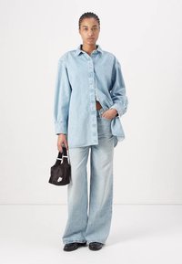 Lyseblå oversized denimskjorte, knappet opp, med matchende vide jeans. Liten svart veske med hvit detalj. Svarte sko fullfører antrekket.