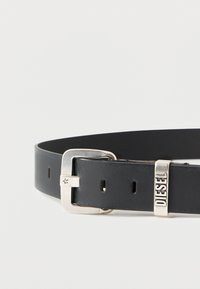 Czarny skórzany pasek z srebrną metalową klamrą i markowym akcentem. Posiada kilka otworów do regulacji rozmiaru. Gładka faktura.