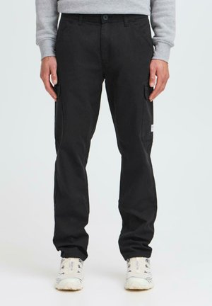 Black cotton cargo pants with a slim fit, featuring side pockets, a buttoned waistband, and a rugged texture. Paired with white sneakers.