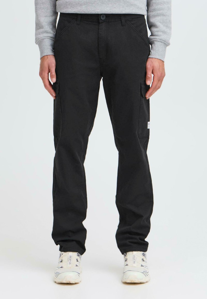 Black cotton cargo pants with a slim fit, featuring side pockets, a buttoned waistband, and a rugged texture. Paired with white sneakers.