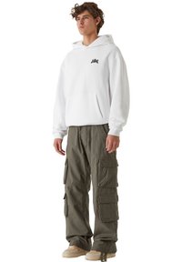 Biała bluza z kapturem z centralną kieszenią i czarnym logo, w połączeniu z oliwkowo-zielonymi spodniami cargo z wieloma bocznymi kieszeniami i luźnym krojem.