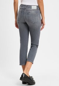 Graue, knöchellange Jeans aus Denim, mit taillierter Passform, zwei Gesäßtaschen und einem minimalistischen Taillenlabel. Kombiniert mit schwarzen Slippern.