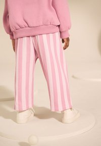 Pantalones de rayas rosas con una textura suave, que presentan piernas anchas y un ajuste relajado, combinados con zapatillas blancas. Vista trasera mostrada.