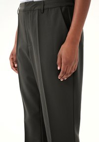 Kalhoty v tmavě olivově zelené barvě, vyrobené z hladkého materiálu. Mají sklady, boční kapsy a přiléhavý střih s rovnými nohavicemi.