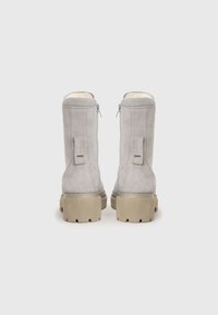Graue Wildlederschuhe mit einem strukturierten Finish, mit Reißverschlüssen hinten und klobigen beigen Sohlen, die ein profiliertes Muster aufweisen.