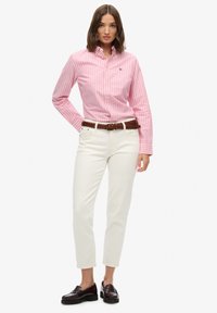 Camicia button-down a righe rosa e bianche con vestibilità slim, abbinata a pantaloni bianchi a gamba dritta, cintura intrecciata marrone e mocassini scuri.