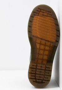 Semelle d'une chaussure en caoutchouc translucide marron avec un motif de bande de roulement texturé, affichant des détails de marque et d'étiquette sur un fond blanc.