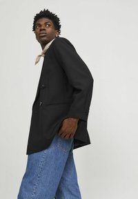 Zwarte dubbelzijdige blazer met een getailleerde pasvorm, met een notch-lapel en twee voorzakken, gedragen over losse blauwe denim jeans.