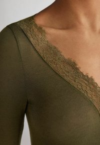 Olive green top with a deep V-neckline, featuring delicate lace trim along the edges. Soft fabric with smooth texture.