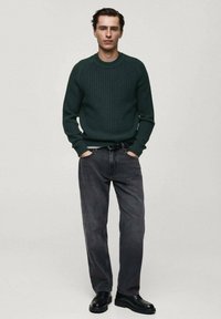 Maglione a coste di colore verde scuro con scollatura rotonda, abbinato a jeans grigi a gamba dritta e scarpe nere con lacci. Design semplice e vestibilità informale.