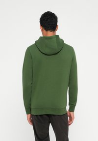 Hoodie vert en tissu doux, avec capuche, poignets côtelés et ourlet droit. La vue arrière montre une coupe décontractée et un design simple.
