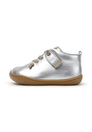 Silberner Leder-Kinderschuh mit beigen Schnürsenkeln, brauner flexibler Sohle und einer Zuglasche an der Ferse, von der Innenseite gezeigt.