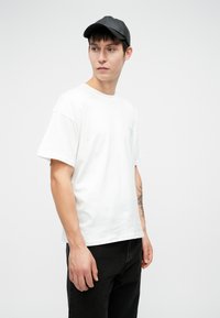 Tricou alb din bumbac, cu maneci scurte și guler rotund, asortat cu pantaloni negri din denim. Căciulă neagră cu o suprafață netedă.